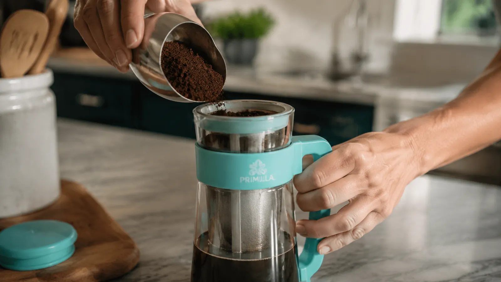 Hand pouring coarse ground coffee into the mesh filter of the Primula cold brew carafe