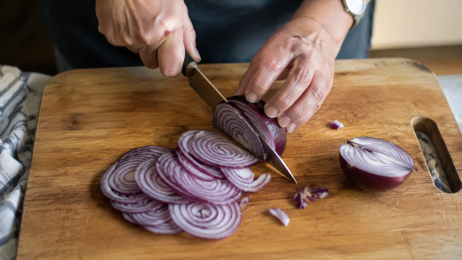 A sharp chef's knife slicing cleanly through a red onion on a wooden cutting board