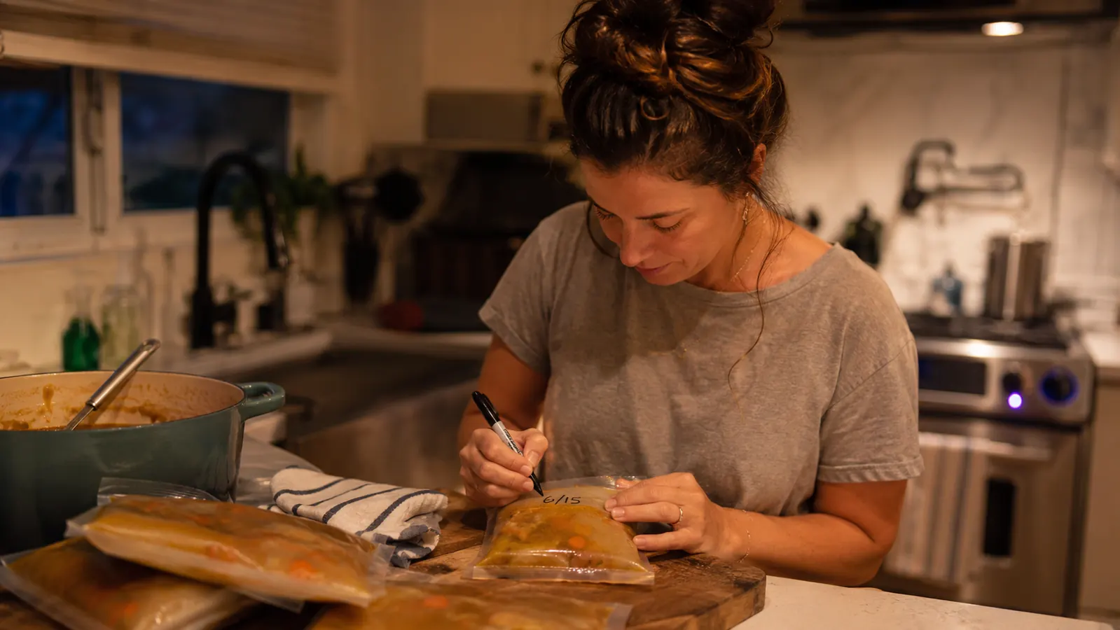 Woman labeling a vacuum sealed bag of soup with a marker before placing it in the freezer