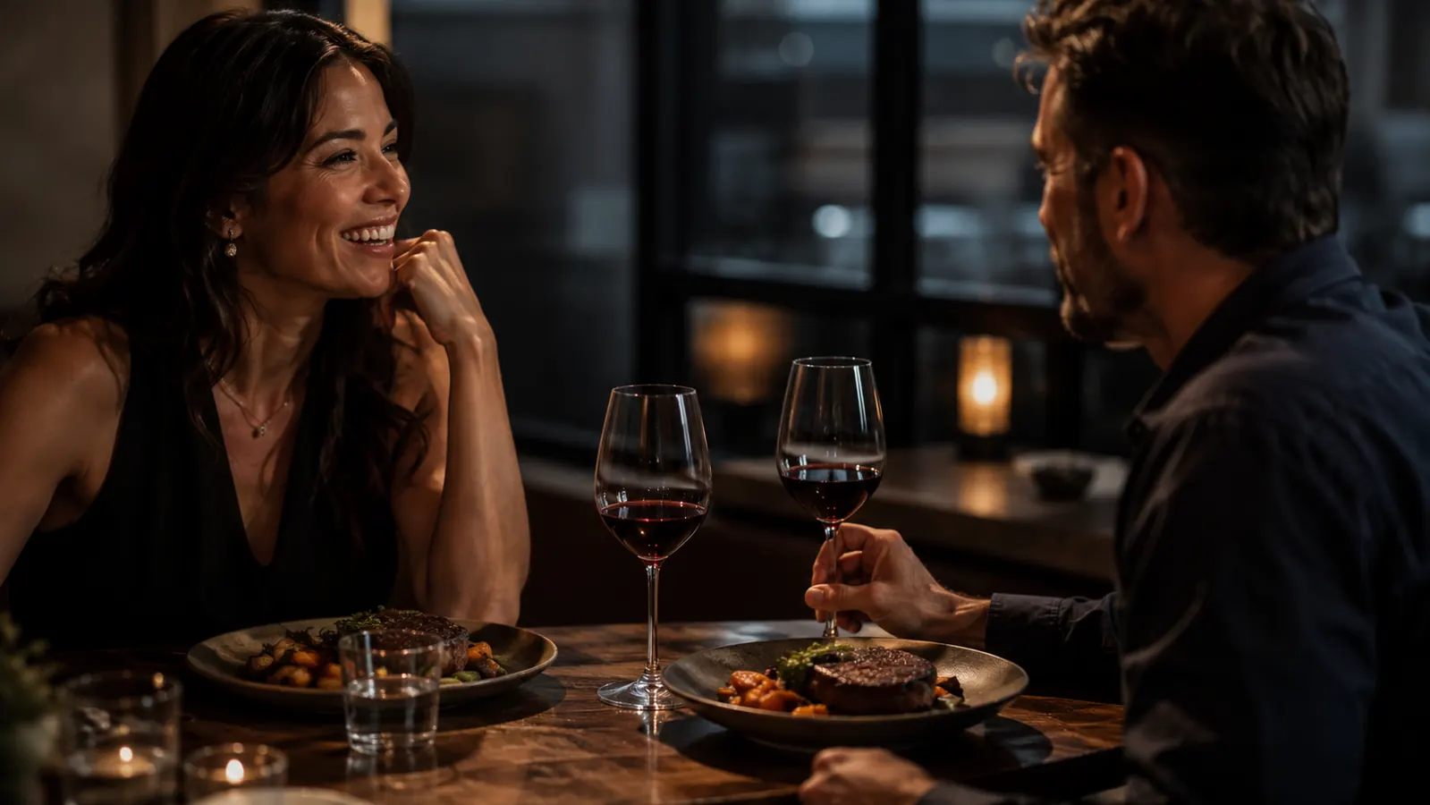 Two glasses of wine and two plates of steak on a small kitchen table set for a quiet dinner at home