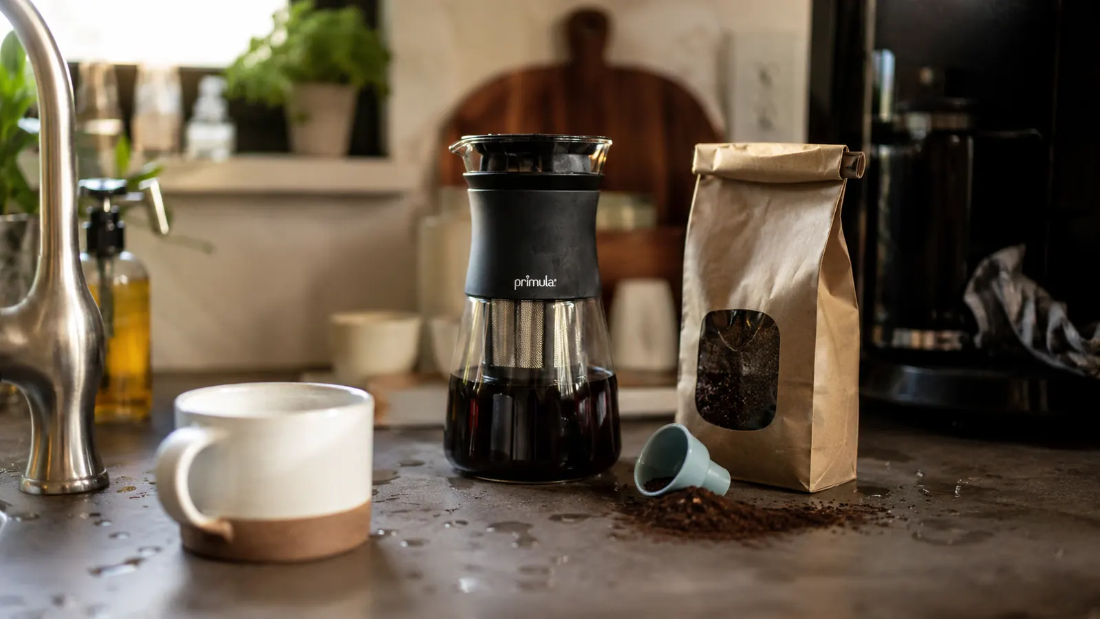 Primula cold brew carafe next to an empty coffee mug and a bag of coarse-ground beans on a counter